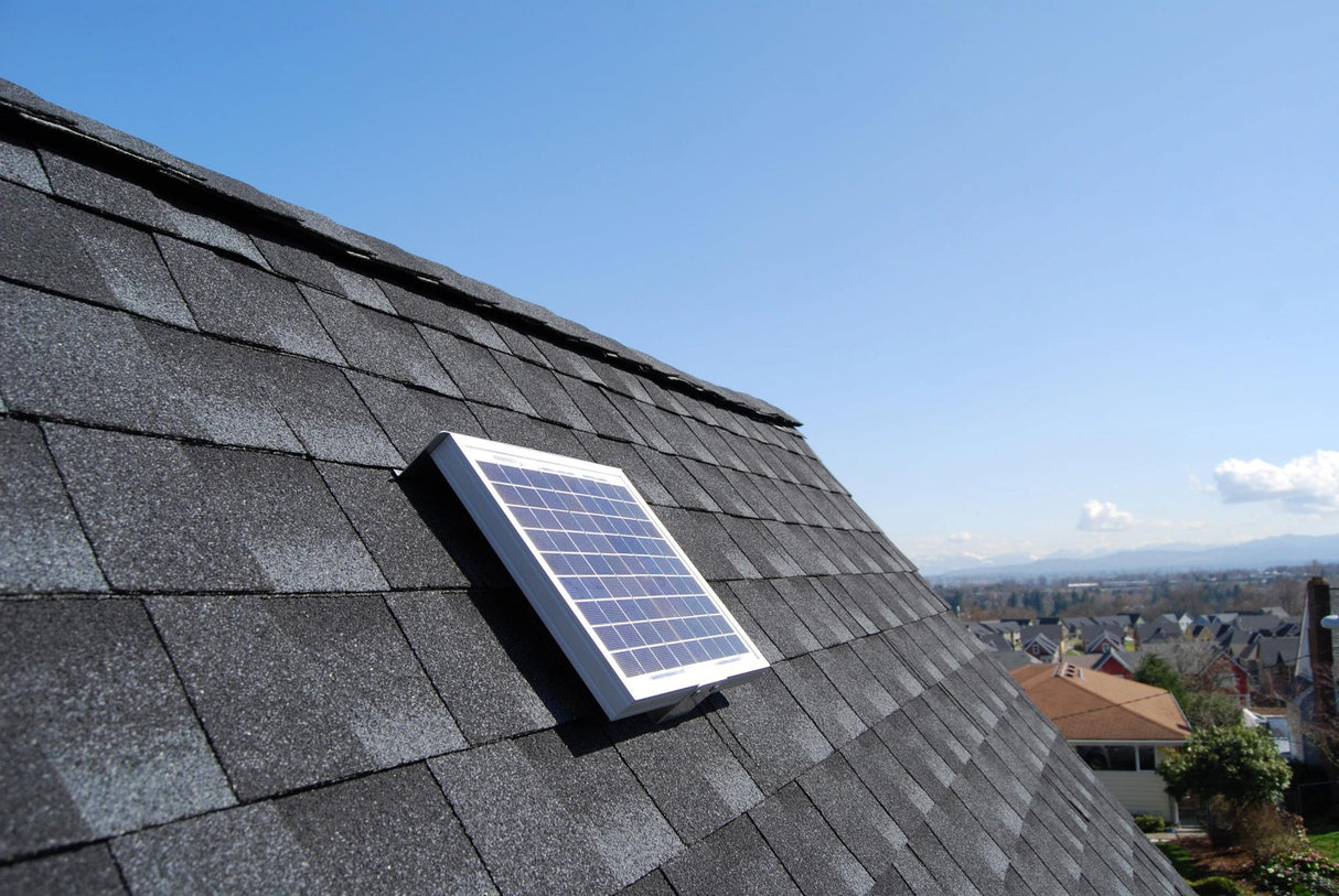 Solar RidgeBlaster has been installed on a steep, dark gray shingled roof of a house with other houses in the background.