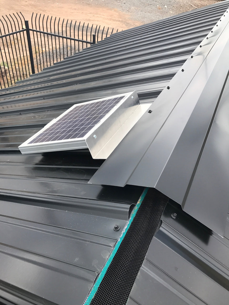 Solar RidgeBlaster has been installed on a dark gray metal roof of a shed with the metal ridge cap being installed as the last step.