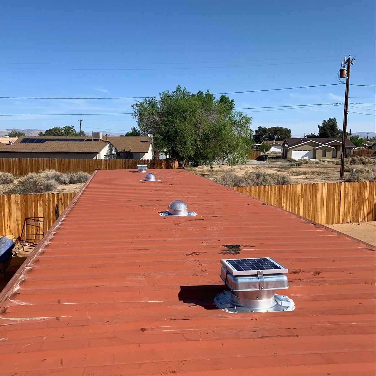 Two Conex Solar Mega Roofblasters and 2 Conex Solar LightBlasters installed on a red shipping container's roof with houses in the background. This is a customer's install photo.