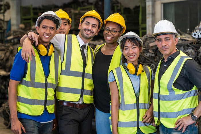 Group of people wearing safety vests and hard hats in an industrial warehouse setting