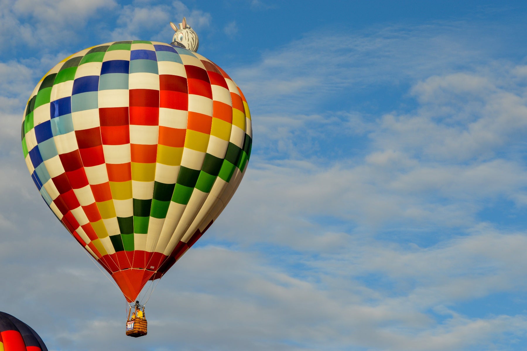 Colorful hot air ballon flying in a slightly cloudy blue sky.