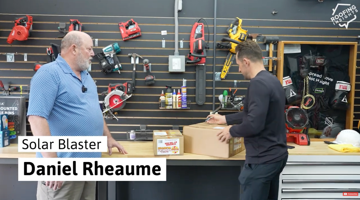 Two men in a workshop setting with tools and equipment on the wall.