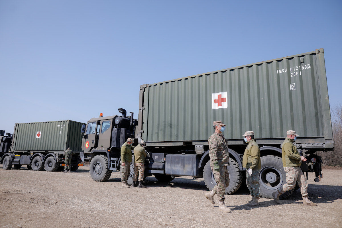 A photo of two military vehicles with shipping containers used for First Aid with six solders in view.