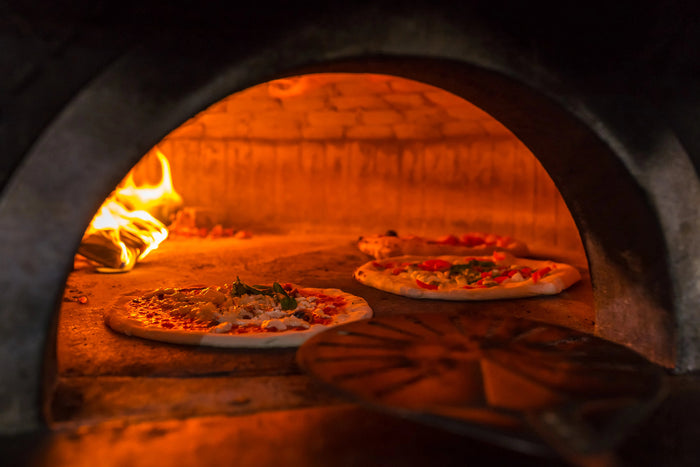 Three pizzas baking inside a wood-fired oven with flames.