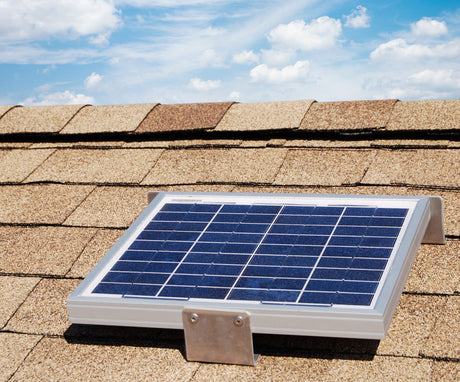 Solar RidgeBlaster has been installed on a brown shingled roof of a house with cloudy blue sky in the background.