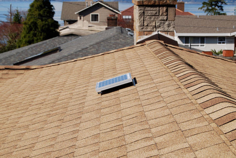 Solar RidgeBlaster has been installed on a brown shingled roof of a house with other houses in the background.