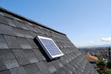 Solar RidgeBlaster has been installed on a steep, dark gray shingled roof of a house with other houses in the background.