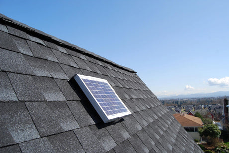 Solar RidgeBlaster has been installed on a steep, dark gray shingled roof of a house with other houses in the background.